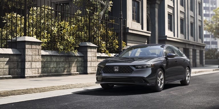 2026 Honda Accord in Meteorite Gray Metallic parked on the street next to a building and a city park with trees.